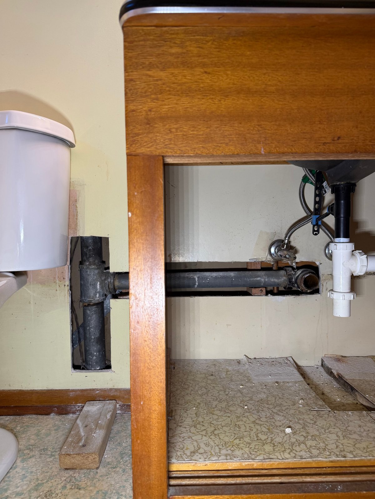 Interior of wooden sink cabinet showing white water container on left and exposed black pipes and white valve on right side